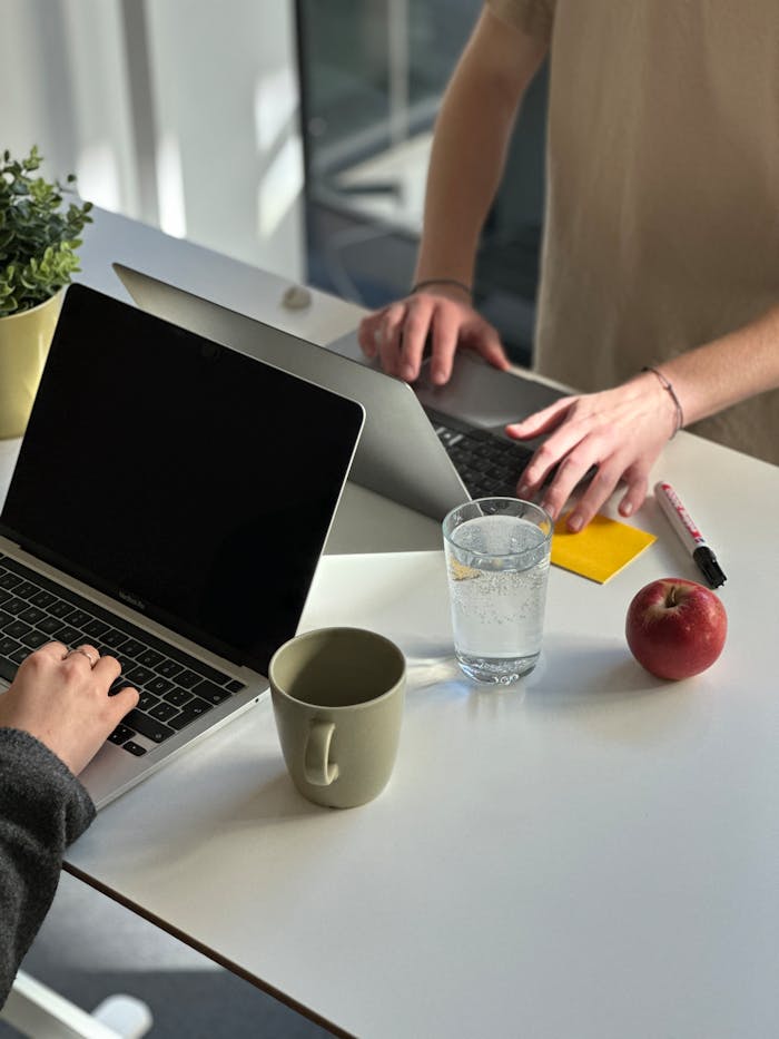 Two people working on laptops at a modern office desk with coffee and an apple.